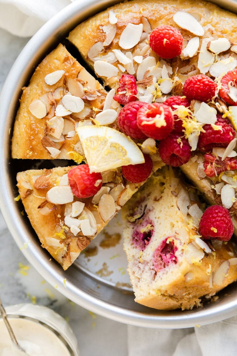 Raspberry lemon coffee cake in round pan, cut into slices, one slice on side to show inside texture.