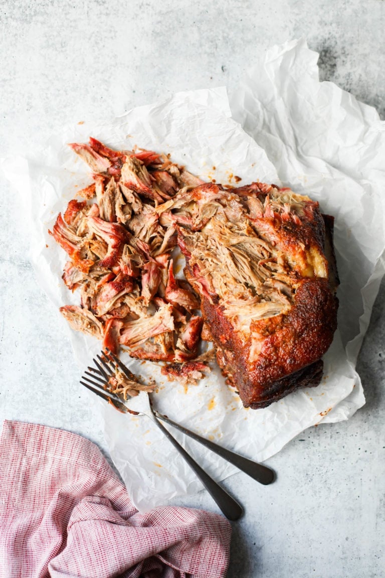 Smoked pork butt partially shredded on white parchment on a countertop