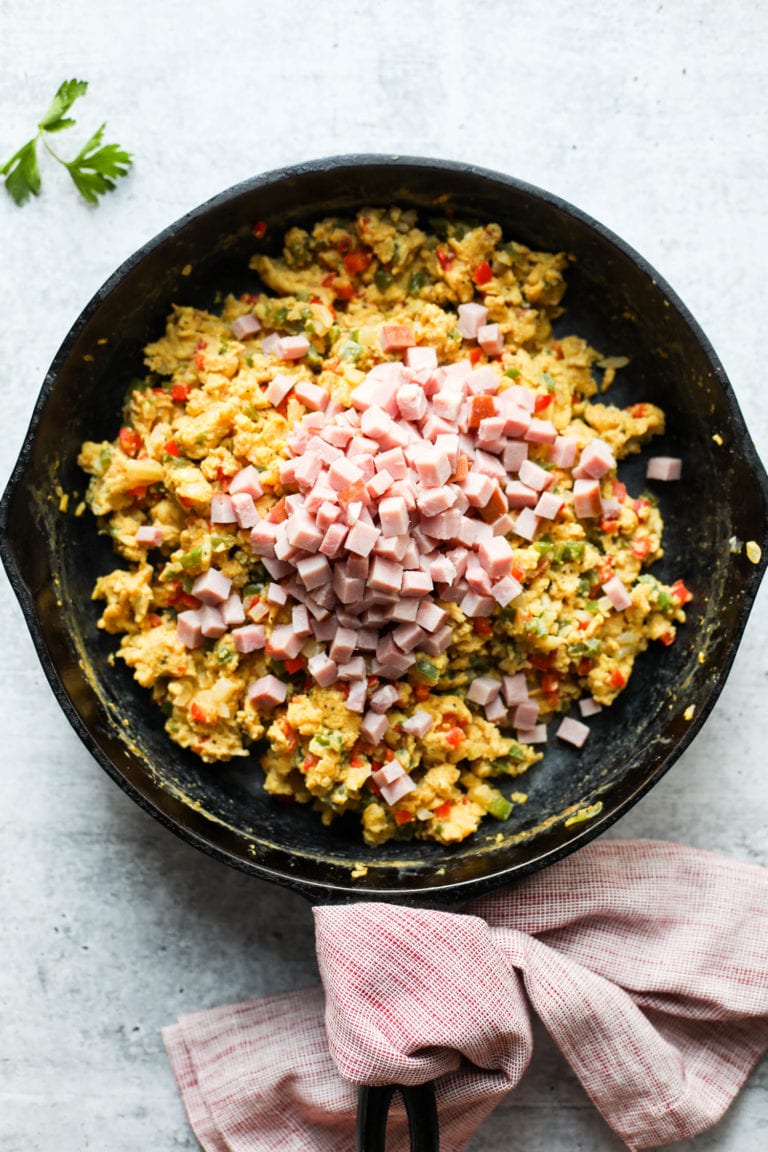 Overhead view of scrambled eggs in a cast iron skillet with diced ham added to the top