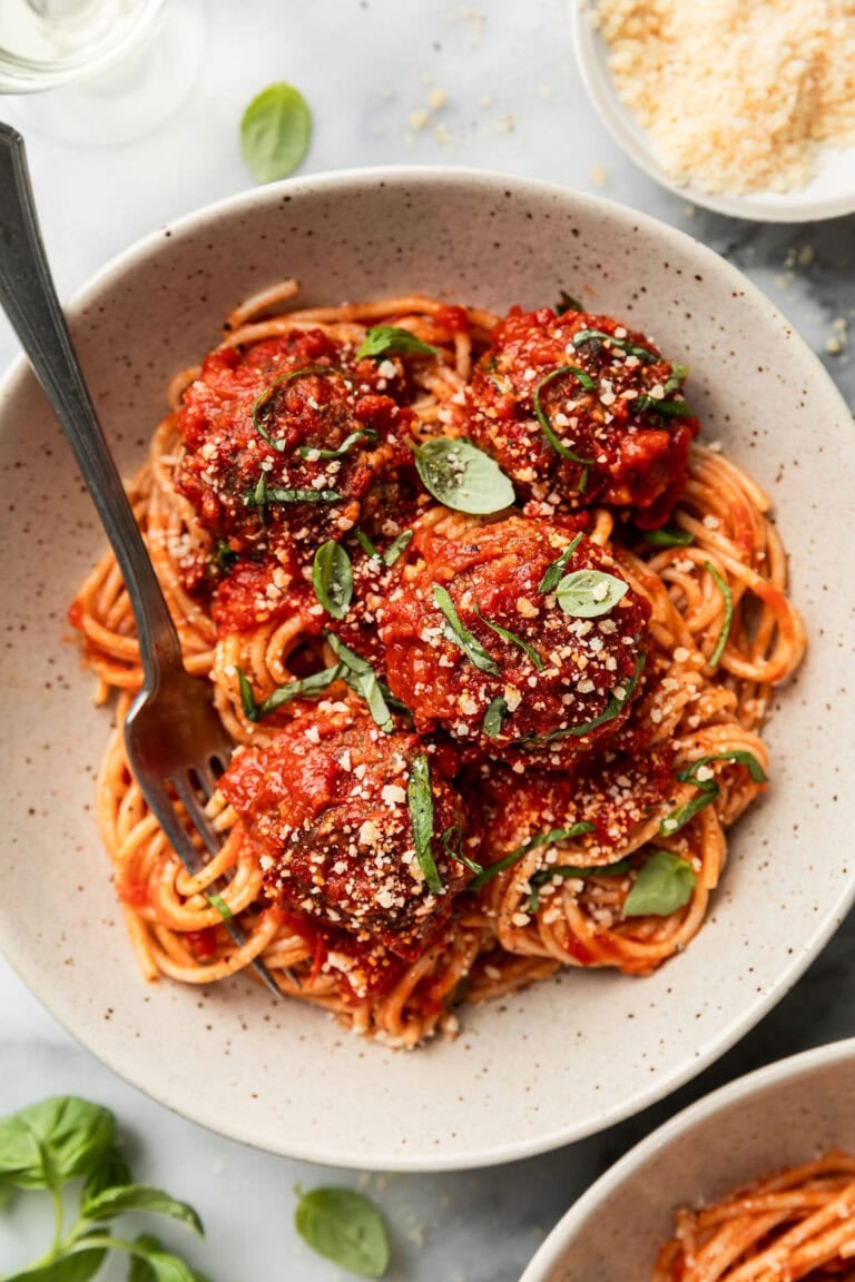 Baked Italian meatballs coated in red sauce over spaghetti noodles in a bowl